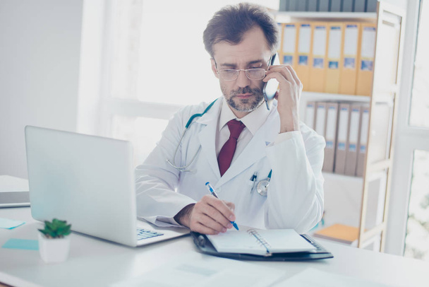 Serious doctor is consulting patient by the phone and writing do - Foto, imagen