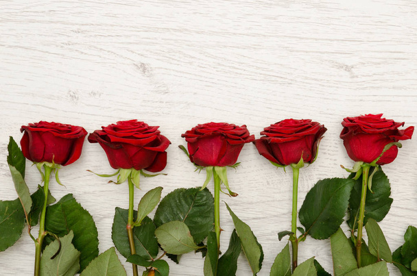 Five red rose on a light wooden background at the edge of the frame, top view. Space for text - 写真・画像