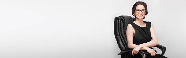 肘掛け椅子に座っている黒のドレスを着た女性  - 写真・画像