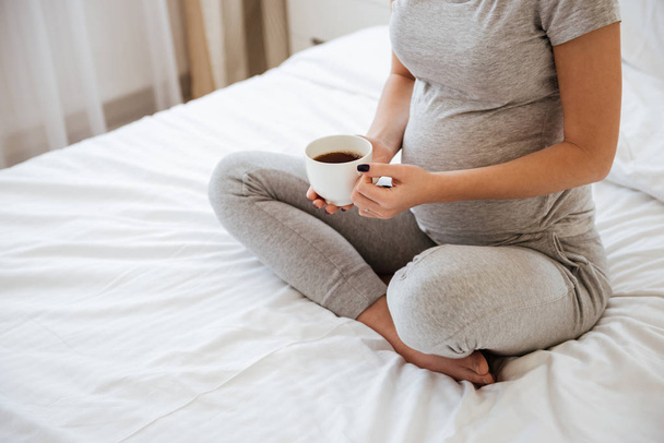 Pregnant woman sitting on bed and drinking coffee at home - Φωτογραφία, εικόνα