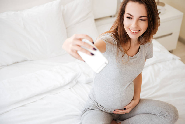 Cheerful pregnant woman sitting and taking selfie with mobile phone - Fotoğraf, Görsel