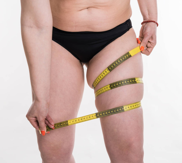 Modelo de mujer de talla grande midiendo su pierna con cinta métrica
 - Foto, Imagen