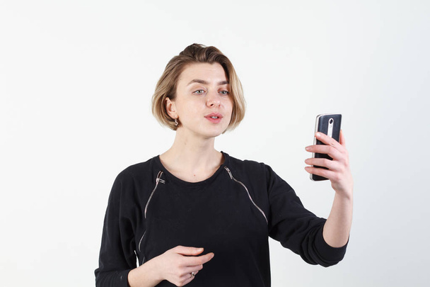 Young beautiful business woman makes selfie on your phone against a white wall - Photo, Image