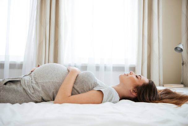 Hymyilevä raskaana oleva nuori nainen makaa ja rentouttava sängyssä
 - Valokuva, kuva