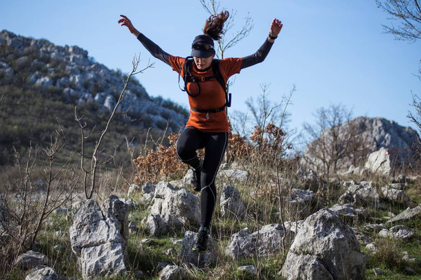 Una mujer con ropa deportiva corriendo y saltando por las montañas rocosas
. - Foto, imagen