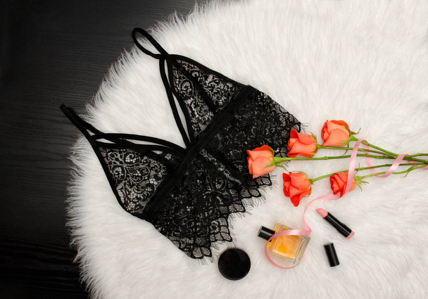 Black lace top on white fur and a bouquet of orange roses and cosmetic. Fashionable concept. Top view - Photo, Image