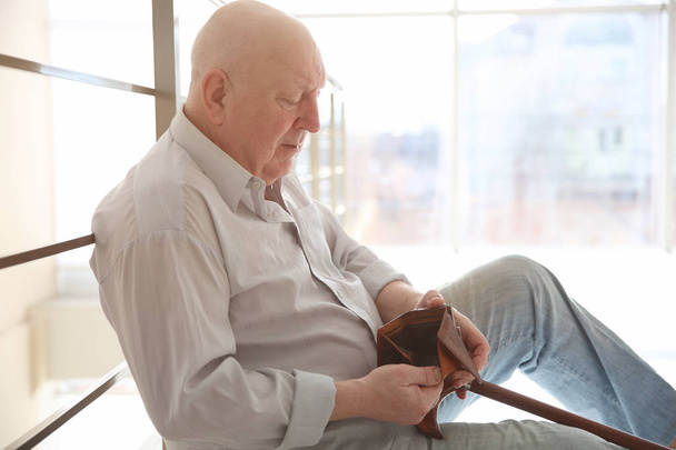 Senior man sitting near banisters with empty purse. Poverty concept - Zdjęcie, obraz