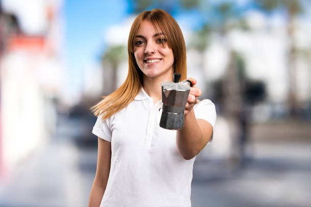 Gelukkig mooi jong meisje die een koffiepot op ongericht achtergrond - Foto, afbeelding