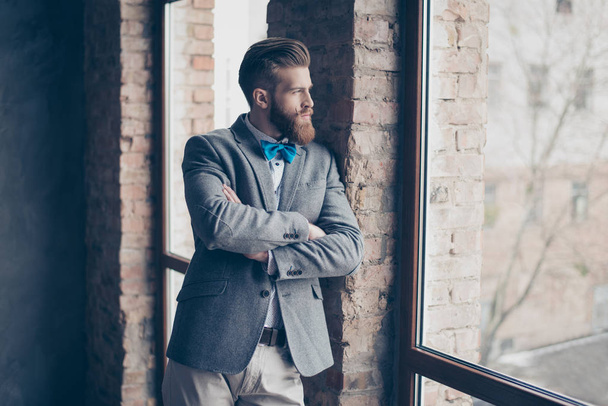 Portrait of young bearded guy with mustache in a suit stands on  - 写真・画像
