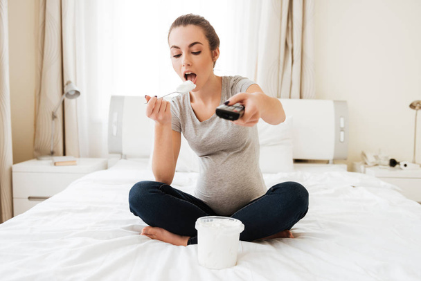 Zwangere vrouw met afstandsbediening eten icecream en Tv kijken - Foto, afbeelding