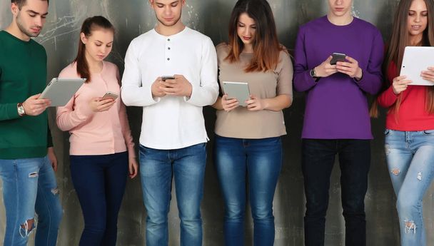 Молоді люди використовують цифрові пристрої на сірому текстурованому фоні
 - Фото, зображення