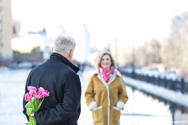 Senior man giving flowers to his wife outdoors - Foto, afbeelding