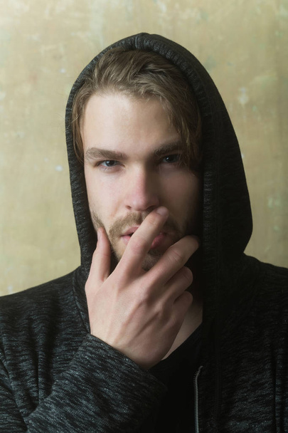 Young man hiding unshaven face with hand wearing grey hoodie - Valokuva, kuva