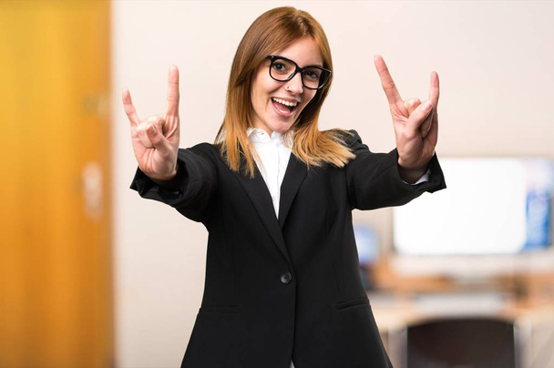 Νέοι επαγγελματίες γυναίκα κάνοντας κέρατο χειρονομία στο γραφείο σε αόριστες φόντο - Φωτογραφία, εικόνα