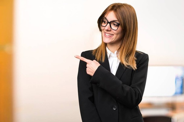 Молодая деловая женщина, указывающая на латеральность в офисе на неориентированном фоне
 - Фото, изображение