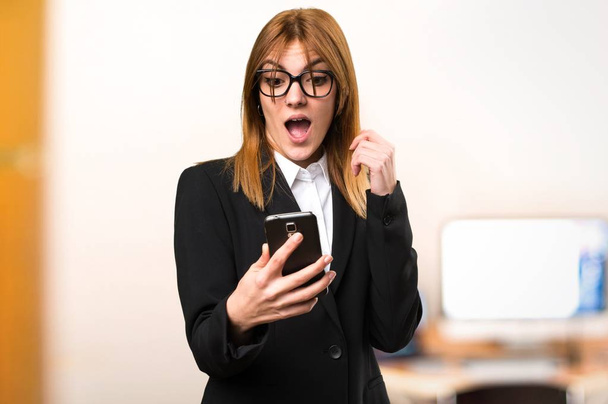 Young business woman talking to mobile in the office on unfocused background - Фото, изображение