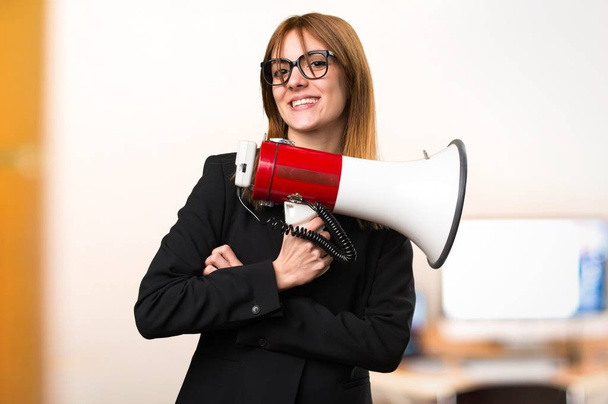 Young business woman holding a megaphone in the office on unfocused background - Zdjęcie, obraz