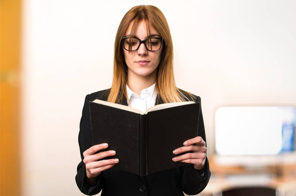 Jonge zakelijke vrouw leesboek in het kantoor op ongericht achtergrond - Foto, afbeelding