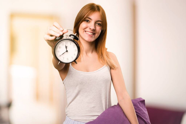 Beautiful girl in pajamas holding vintage clock inside a room - Foto, Imagem