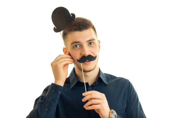 young handsome guy keeps near the face, paper mustache and a hat - Zdjęcie, obraz
