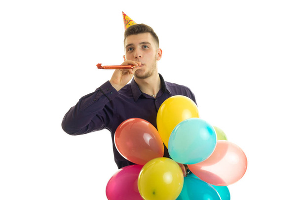 бодрый молодой парень с конусом на голове держит возле рта dudelku и много цветных воздушный шар
 - Фото, изображение