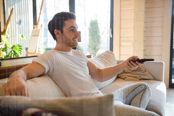 Sideview of sitting on couch man with remote controller - Photo, Image