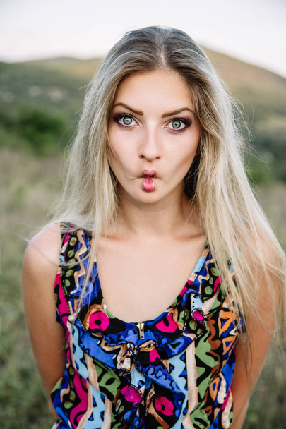 Beautiful blonde with beautiful eyes in blue overalls in nature, sunset sun - Zdjęcie, obraz