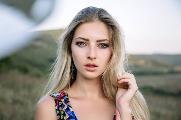 Portrait of a beautiful blonde with beautiful eyes in blue overalls in nature, the setting sun - Photo, Image