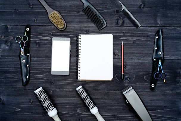 Hairdresser tools on wooden background. Blank card with barber tools flat lay. Top view on wooden table with scissors, comb and hairclips with empty notebook, pencil and phone, free space - Foto, Bild