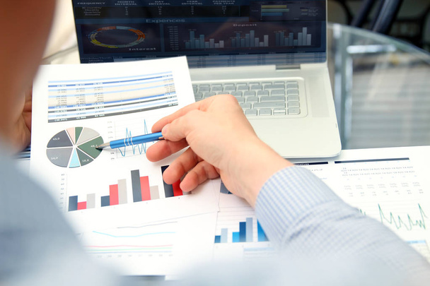 Homem de negócios trabalhando e analisando figuras financeiras em um gráfico usando laptop
 - Foto, Imagem