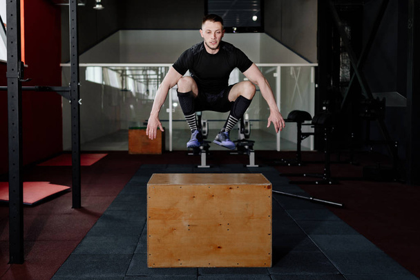 Fit young man jumping onto a box as part of exercise routine. Man doing box jump in the gym. Athlete is performing box jumps  - Photo, image