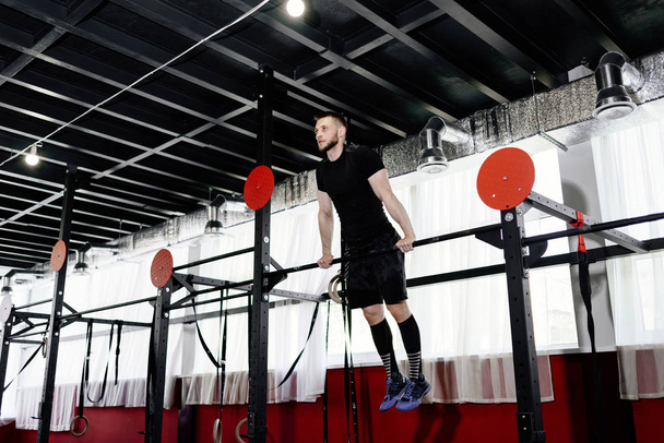Young man exercising on horizontal bar in the gym. Male adult working out triceps and biceps on horizontal bar  - Фото, зображення