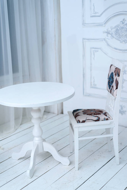 Mesa redonda de madera blanca con una silla en el interior cerca de la w
 - Foto, Imagen