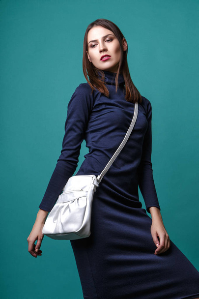 Fashion shot of a woman in blue drees with white bag in studio on green background - Foto, Imagem