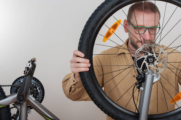 Bärtiger Mann legt Vorderrad aufs Fahrrad. - Foto, Bild