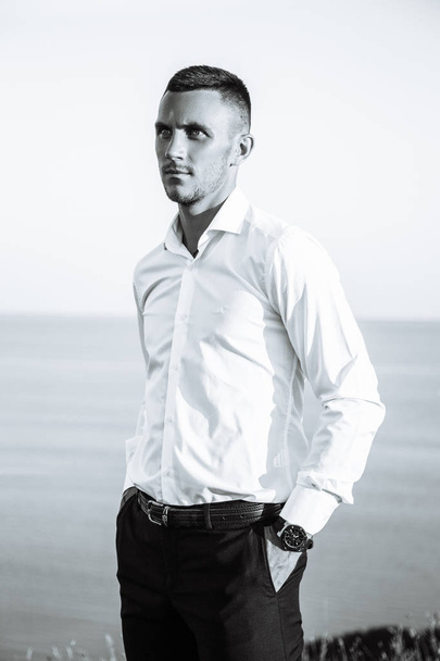 Cheerful young man athlete in white shirt standing near the sea. Black and white - Valokuva, kuva