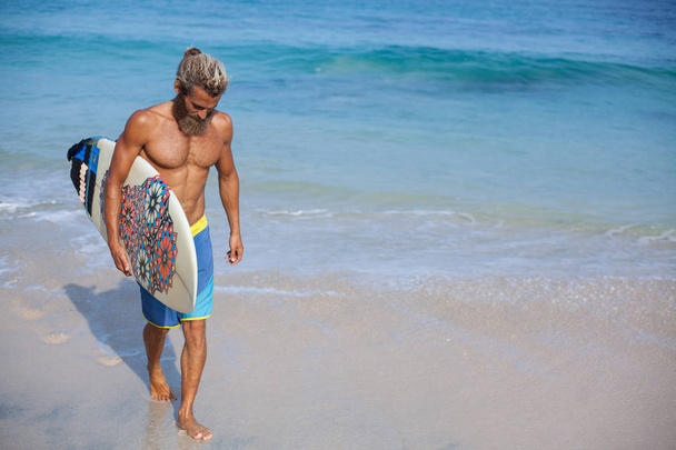 muotokuva houkutteleva parrakas kihara mies surffilauta kävelee rannalla, joka sijaitsee vasemmalla puolella runko
 - Valokuva, kuva