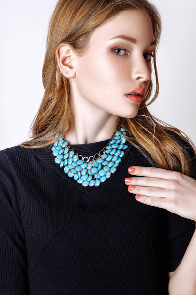 Fashion portrait of beautiful young woman with blond hair. Girl in a black dress and blue necklace on a white background - Φωτογραφία, εικόνα