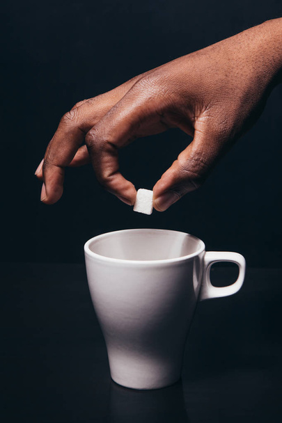 Black man hand hold cube of sugar above white cup - Fotoğraf, Görsel