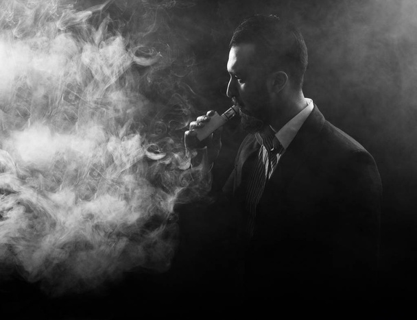 Vaping man holding a mod. A cloud of vapor. Black background. - Photo, Image
