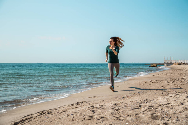 Κορίτσι σε αθλητικά ενδύματα που τρέχει κατά μήκος της θάλασσας - Φωτογραφία, εικόνα