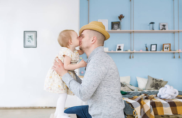 Bonito jovem pai está beijando sua menina bonito. Ambos estão no quarto em casa
 - Foto, Imagem