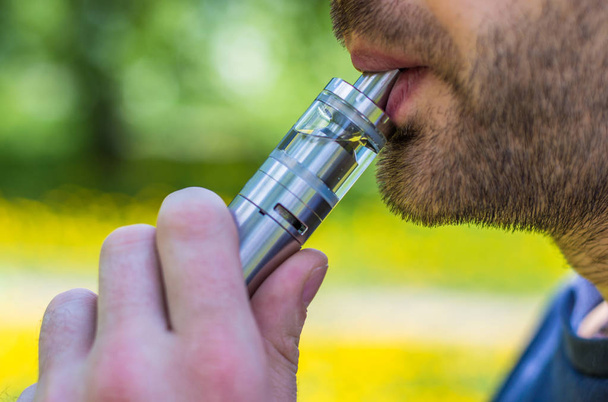 Adult man smoking a vape e-cigarette in the park - Фото, зображення