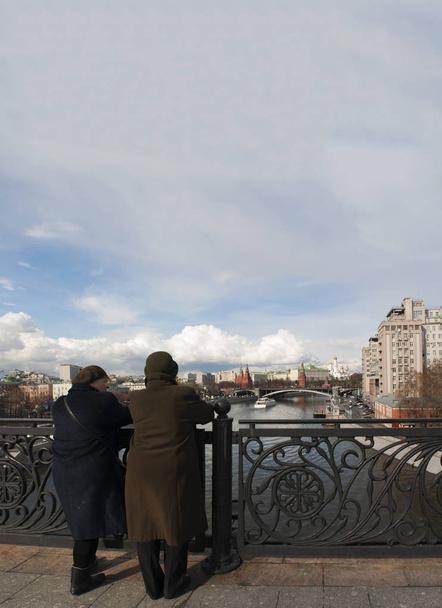 Russia: two old Russian women looking the skyline of Moscow with view of the fortified complex of the Kremlin from the Patriarch Bridge on the Moskva River  - Photo, Image