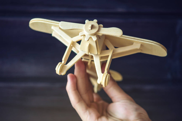 Hand holds Wooden toy plane that flies on a dark background in retro style - 写真・画像