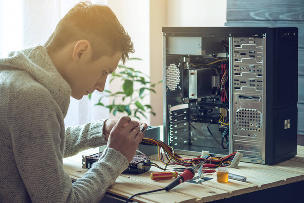 Человек-ремонтник пытается починить с помощью инструментов на компьютере, который находится на рабочем месте в офисе
 - Фото, изображение