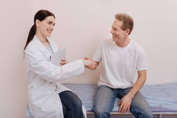Friendly delighted doctor shaking hands with a patient - Photo, Image