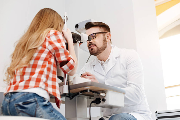 Concentrated diligent ophthalmologist observing patients eyes - Foto, Imagen