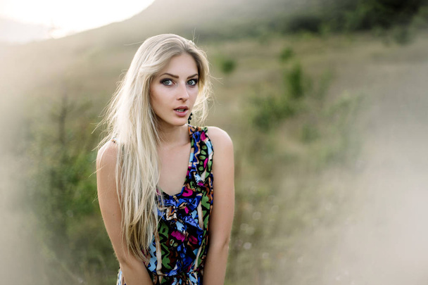 Beautiful blonde with beautiful eyes in blue overalls in nature, sunset sun - Photo, Image
