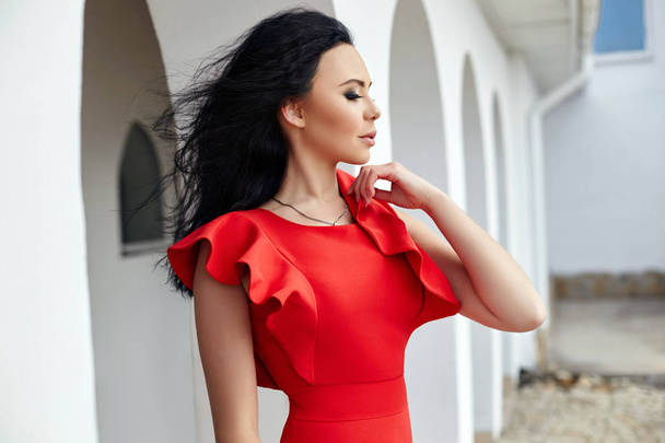 Sexy brunette woman in red dress stands near the walls of the ol - Фото, зображення